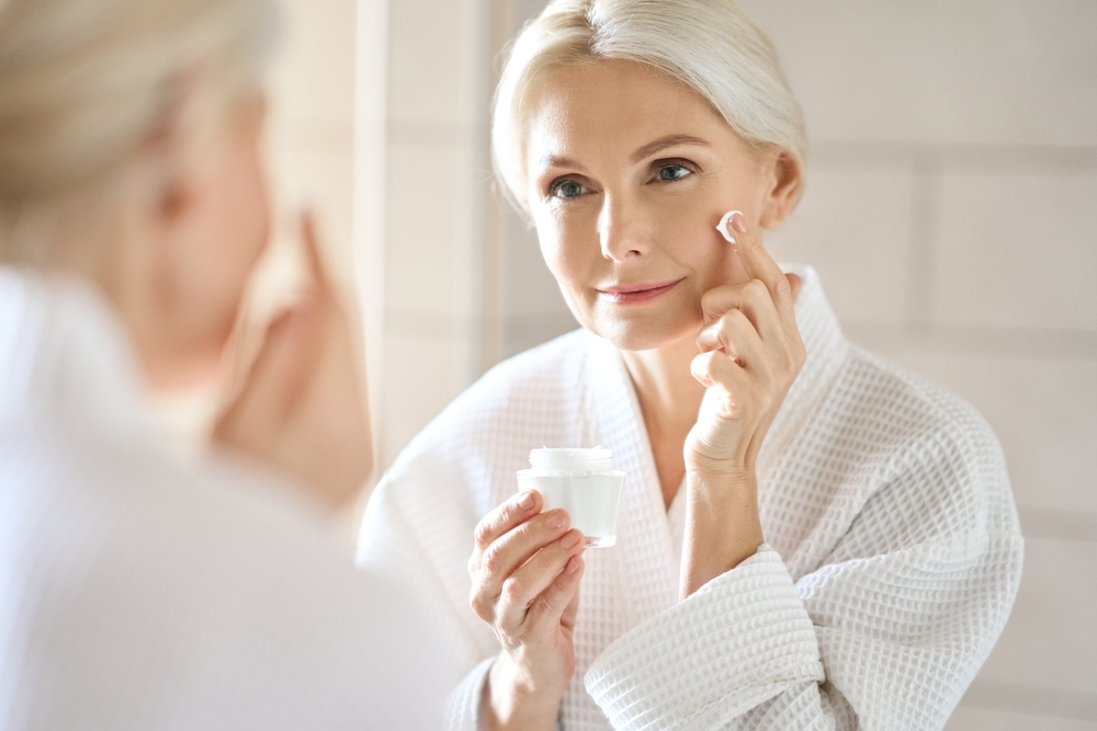 A mature woman applying skincare for aftercare following biostimulators treatment.