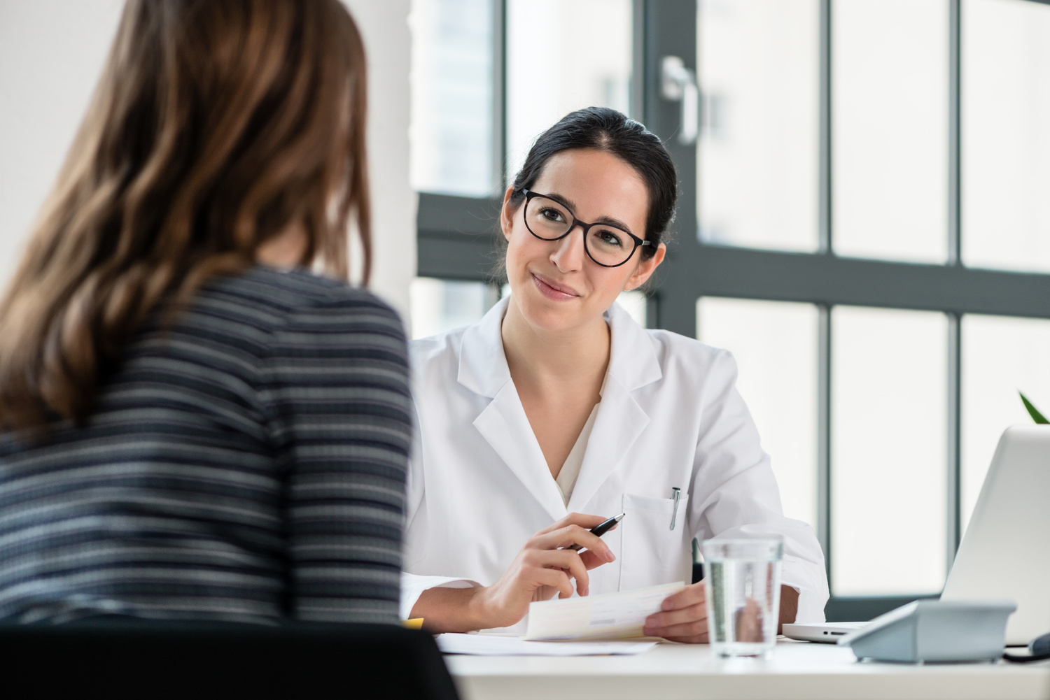 Healthcare provider seated at a desk speaking with a patient across from her in an office