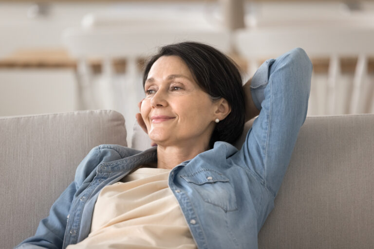Woman reclining on a sofa with arms resting behind her head in a softly lit living room
