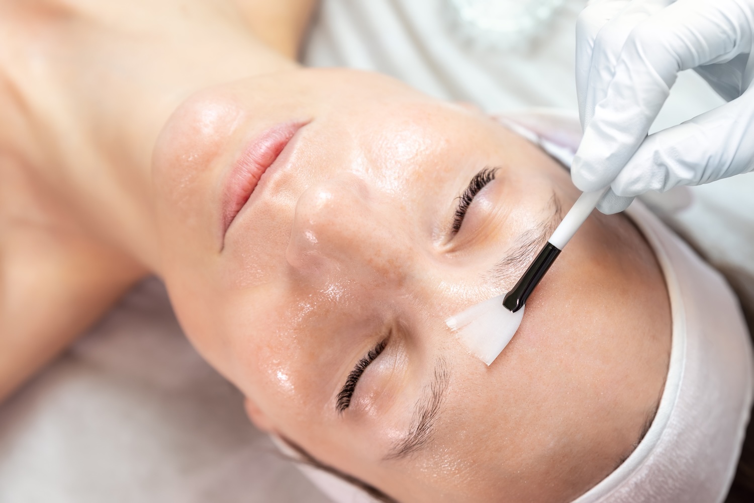 Esthetician applying serum to woman's forehead during facial treatment