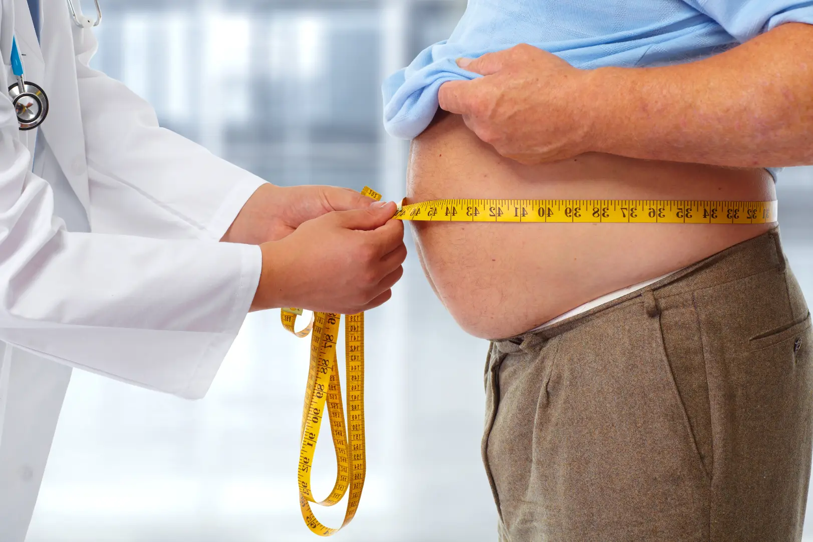 Doctor measuring a man’s waist with a tape measure during a checkup