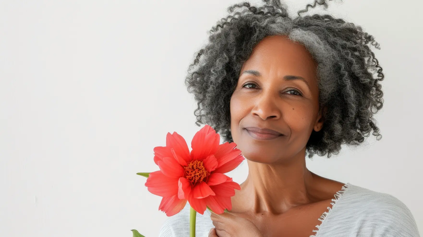 Older woman holding a red flower and smiling at the camera