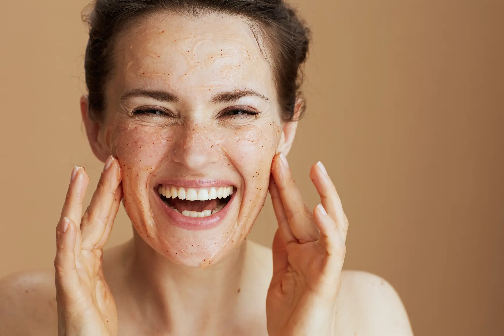 Woman smiling while applying grainy facial scrub to her cheeks