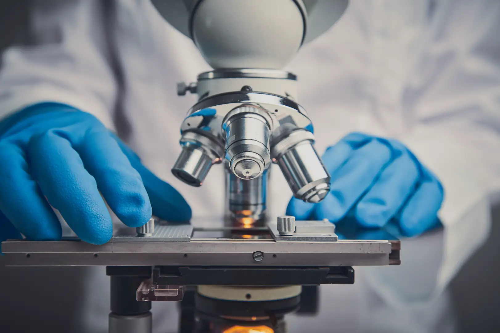 Scientist wearing blue gloves using a microscope in a laboratory.