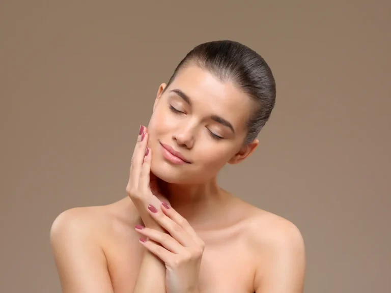 Person with eyes closed touching cheek against a neutral background.