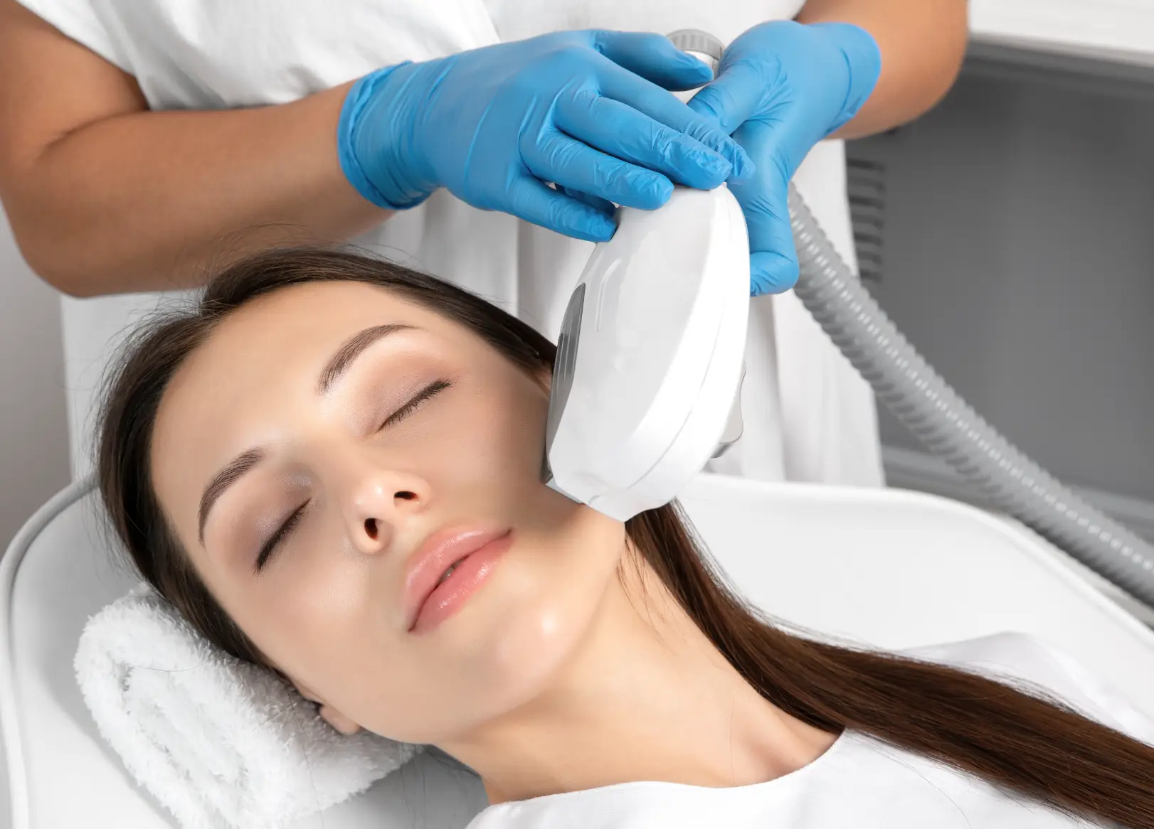 Practitioner uses a laser treatment device on a person's jawline while they rest with eyes closed.