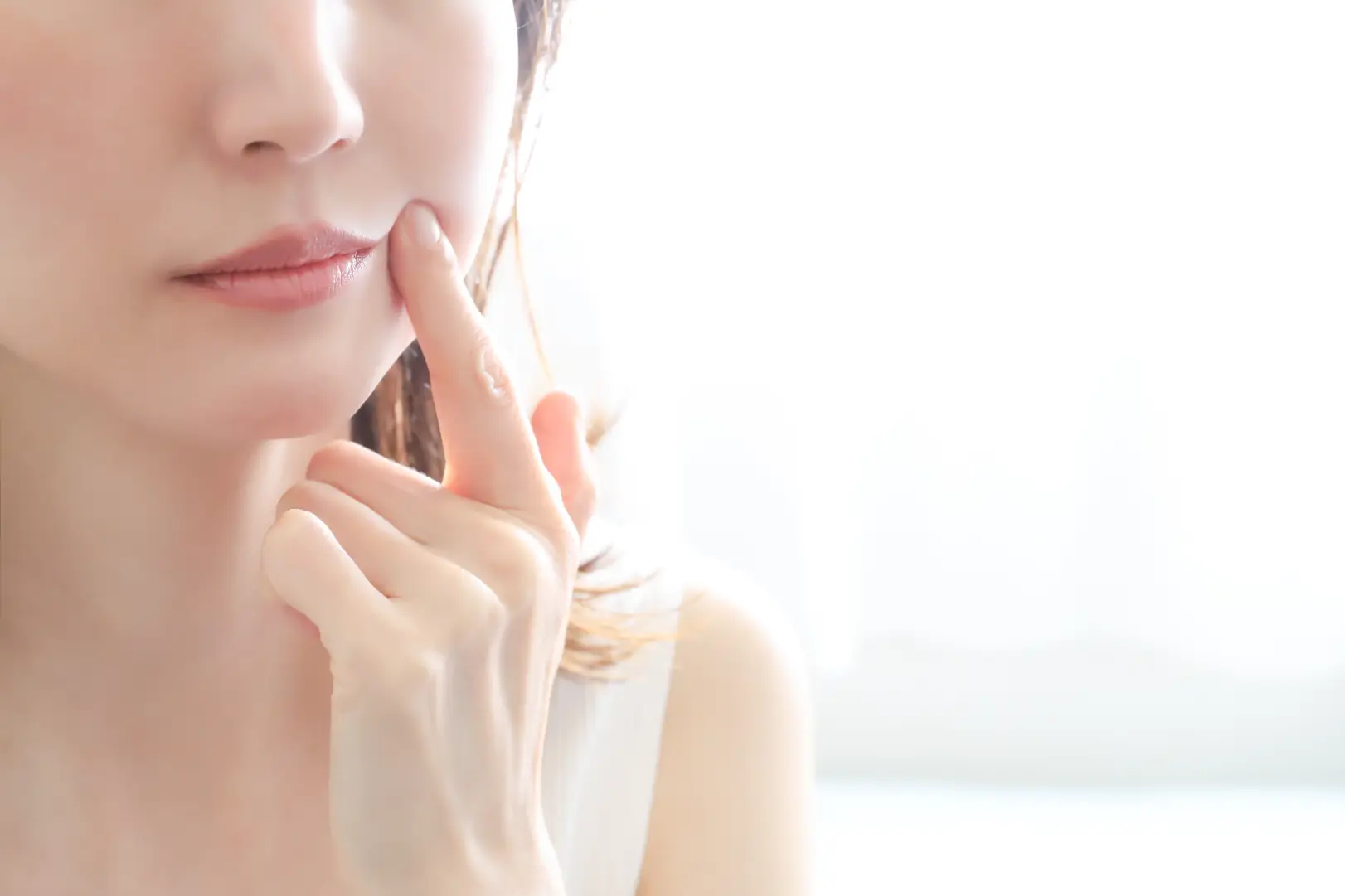 Close-up of a person touching their cheek with one finger in soft natural light.